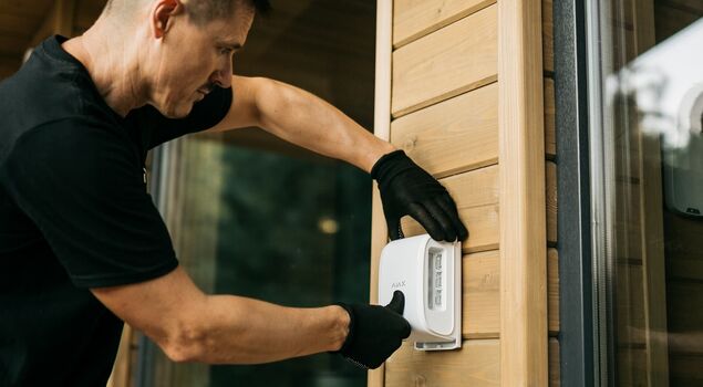 Ein Techniker installiert an einer Holz-Außenwand eine Einbruch­melde­anlage